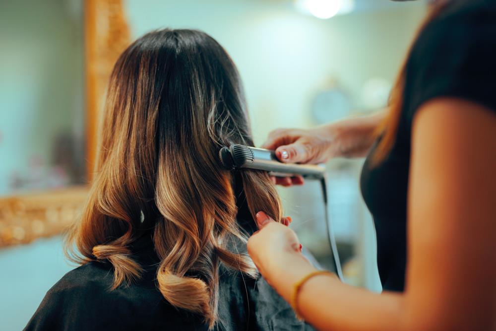 Hairstylist using hair straightener for curling hair in a salon